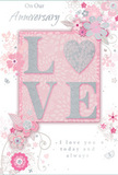The design of this anniversary card feels like a quiet celebration of shared years in Cockfosters, captured in soft pinks and silvered light. At the centre sits the word LOVE, rendered in sturdy capital letters that are slightly raised from the card's surface. A light dusting of glitter wraps each letter, creating a gentle sparkle that shifts as if candlelight were moving across it. This central word rests upon a blush pink panel, bordered by bands of creamy white and touches of subtle silver, giving the impression of layers, much like the stacked petals in an expertly composed bouquet from Cockfosters Flowers. Surrounding the central motif is a cascade of stylized blossoms, fine tendrils, and delicate leaves. The flowers are drawn in a lyrical style, with slim outlines and faint shading in blush, ivory, and soft grey tones that bring to mind spring flowers in the gardens around Trent Park. Some petals and leaves catch hints of silver, adding a faint metallic glimmer that feels refined rather than flashy. The background wash of pale pink unifies the composition, allowing the florals and lettering to appear as if they are gently floating. Interwoven with the botanical details, graceful script text carries anniversary wishes and loving sentiments in a flowing, cursive hand that echoes the curves of the vines. The overall mood is tender and intimate, like a handwritten love note tucked into a bouquet delivered to a doorstep off Cockfosters Road. With its combination of tactile raised glitter, soft pastel colours, and intricate floral illustration, this card offers a visual and textural experience designed to honour enduring romance and cherished memories.